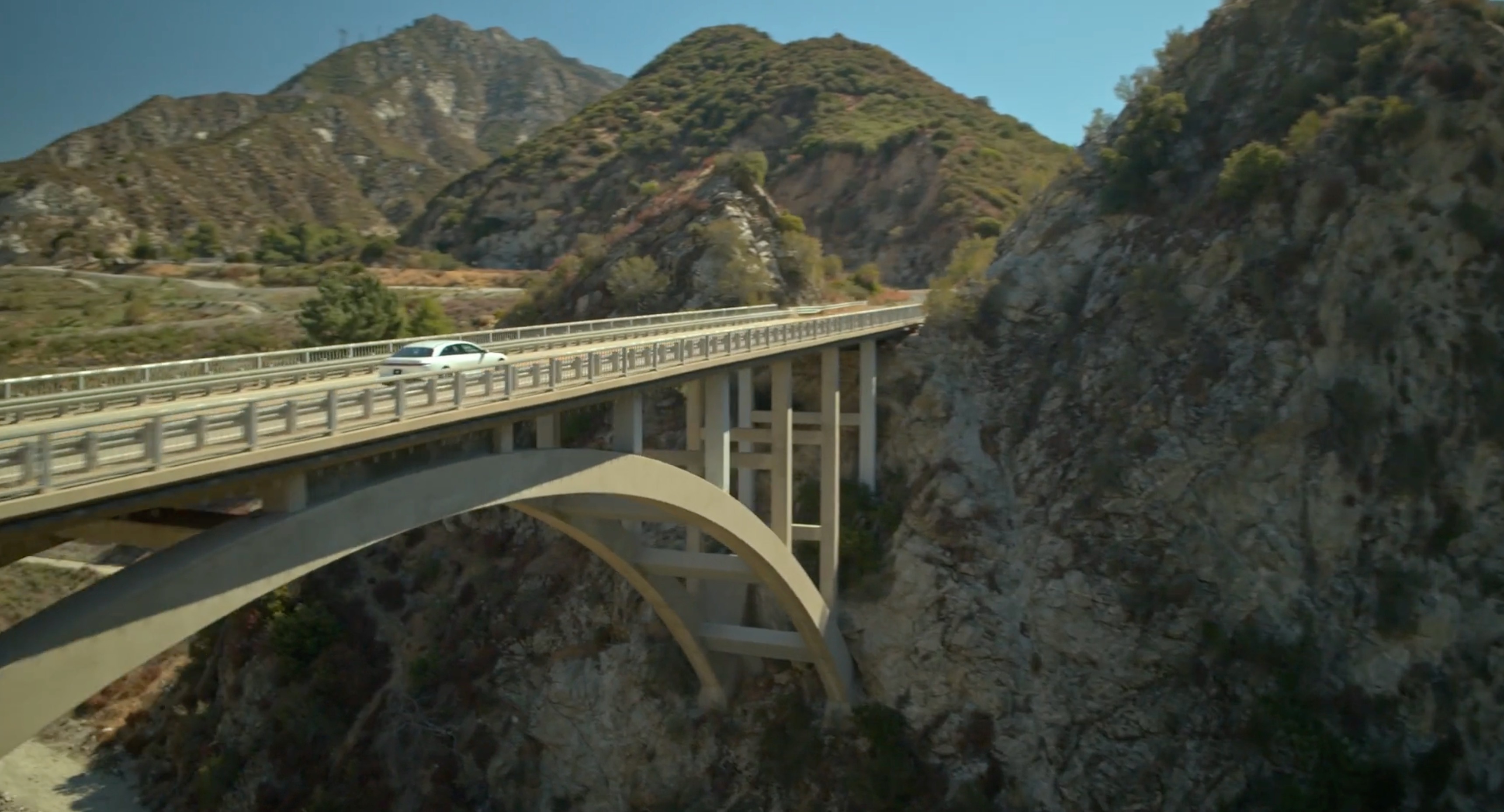 A white car drives across an arch bridge